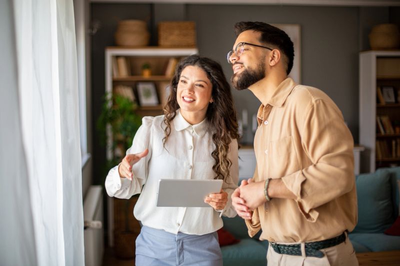 Real estate professional presenting a property to a client using a tablet, highlighting features through a window view