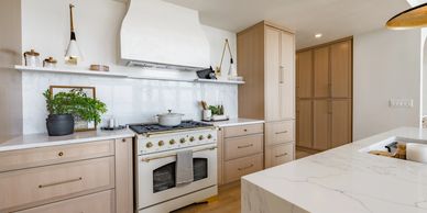 Modern kitchen with light wood cabinets and white marble countertops.
