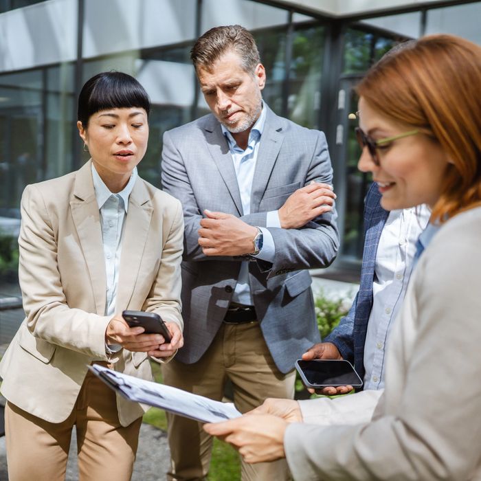 Business professionals reviewing documents and phones outdoors in a discussion.