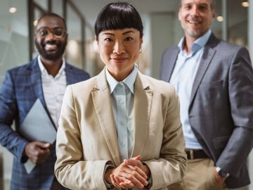 Confident businesswoman with two male colleagues smiling behind her.