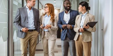 Four professionals walk and talk in a modern office corridor.