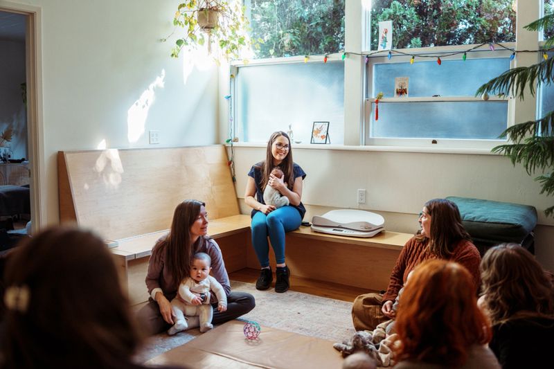 A doctor of physical therapy who specializes in pregnancy, postpartum, and infant development, holds a client's baby while leading a support group for new moms.