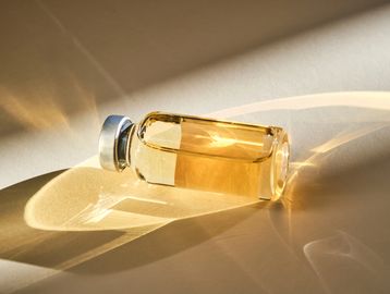A vintage glass vial filled with amber liquid casting intricate shadows.