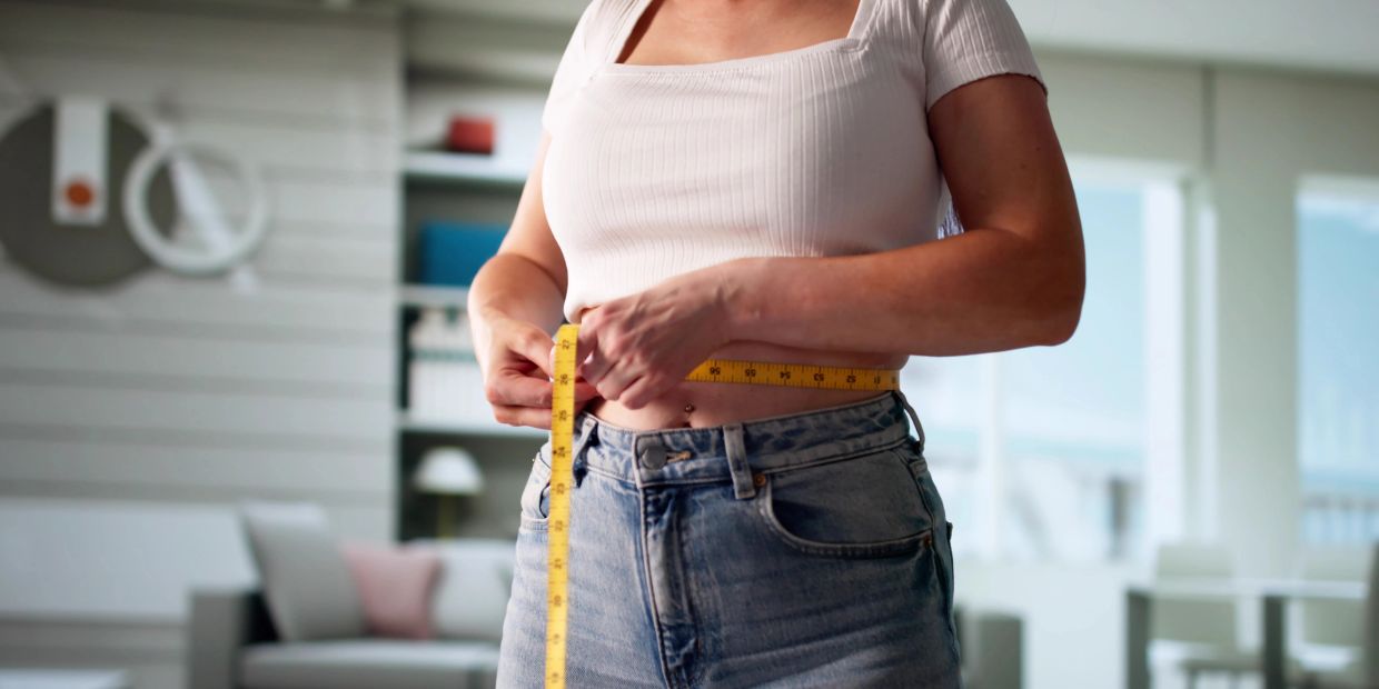 Person measuring waist with a tape measure.