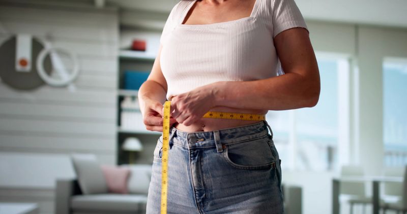 Portrait Of Young Woman Measuring Weight Loss Progress With Tape Measure, Smiling With Satisfaction