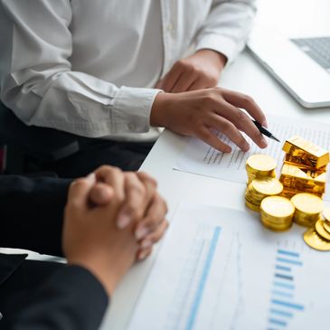 Two people discussing investment with gold bars and coins on the table.