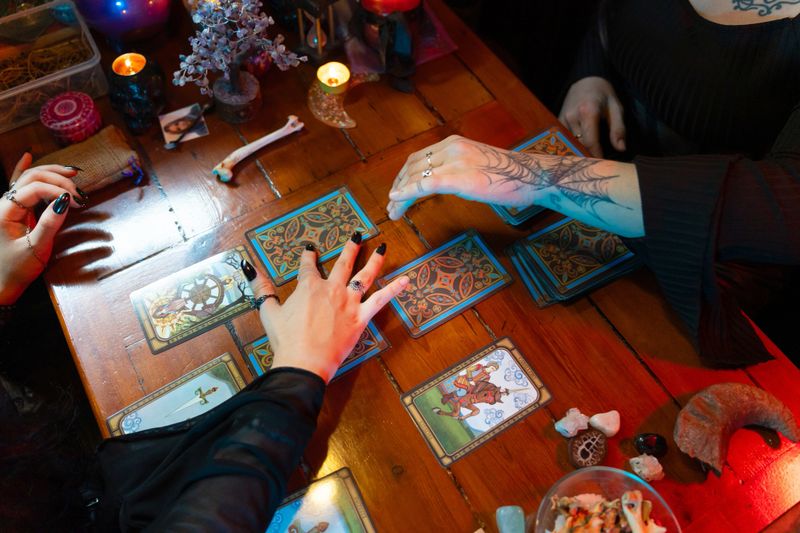 Two fortune tellers reading tarot cards spread on a wooden table, surrounded by candles, crystals, and occult objects, creating a mystical atmosphere