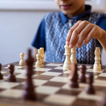 Child playing chess, moving a white queen piece.