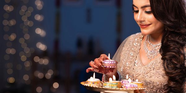 Woman in traditional attire lights decorative candles, smiling serenely.