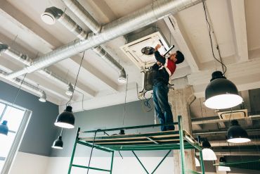 Worker repairing ceiling air conditioning unit on scaffolding.