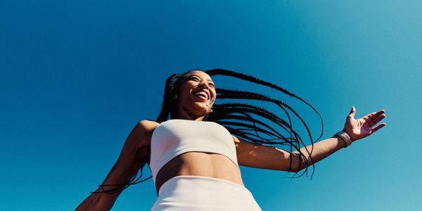 Joyful woman with braided hair enjoying a sunny day against a clear blue sky.