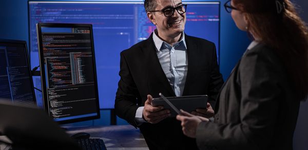 Two professionals discussing in front of computer screens with code.