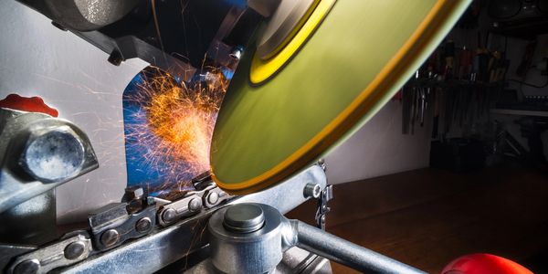 Close-up of a chainsaw chain being sharpened with sparks flying.