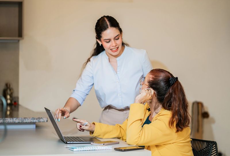 Young professional assists a fellow mayor in front of a laptop in a collaborative work environment.