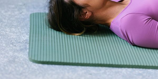 Person lying on a green yoga mat wearing a purple top.