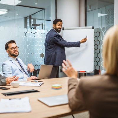 Man in suit presenting with a flip chart in a modern office meeting.