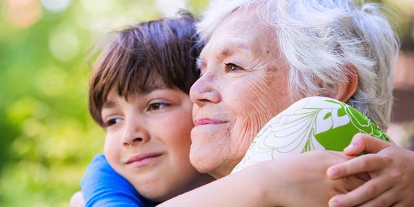 A young boy warmly hugging an elderly woman outdoors, sharing a tender moment.