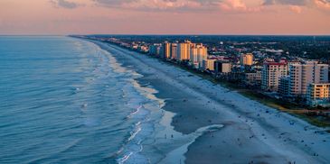 Sunset view of a beach with waves and city buildings along the shore.