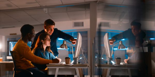 Three colleagues collaborating over a computer in a modern office at night.