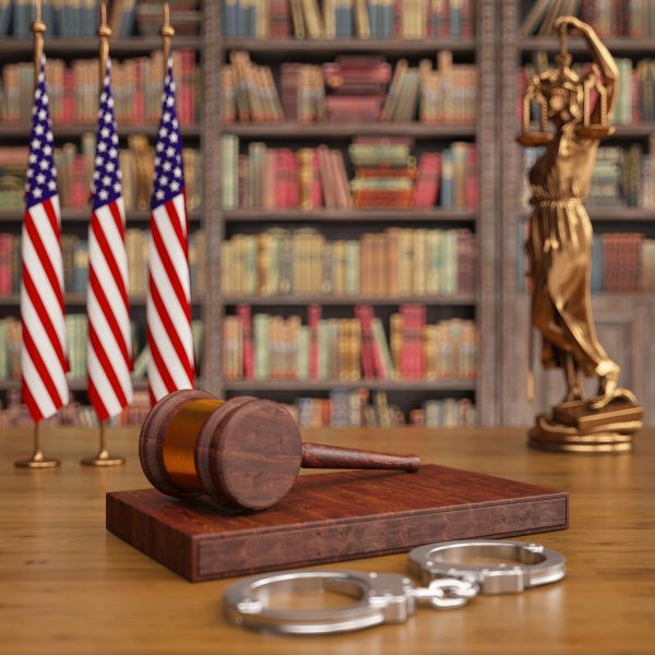 Mazo judicial, esposas y bandera estadounidense en biblioteca legal.