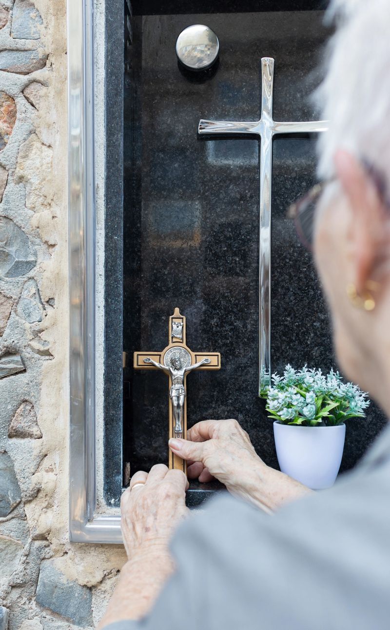 Senior woman placing a wooden crucifix on a tombstone in a cemetery, honoring the memory of the deceased with deep respect and heartfelt remembrance amidst a serene setting