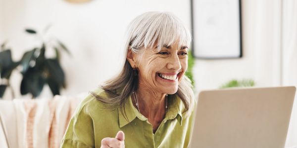 Elderly woman happily video chatting on laptop at home.