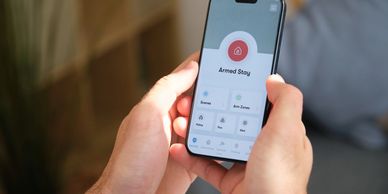Smartphone displaying a home alarm system set to Armed Stay mode using a security monitoring app