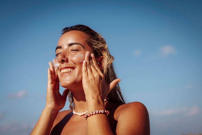 A cheerful woman with tanned skin applies sun cream on her face under the bright tropical sun