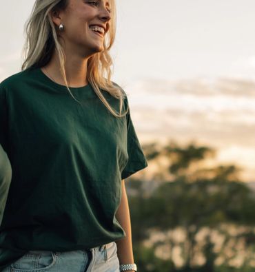 Smiling woman in green shirt outdoors at sunset.