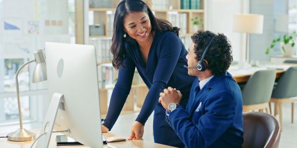 Two colleagues smiling and discussing work at a computer in a bright office.