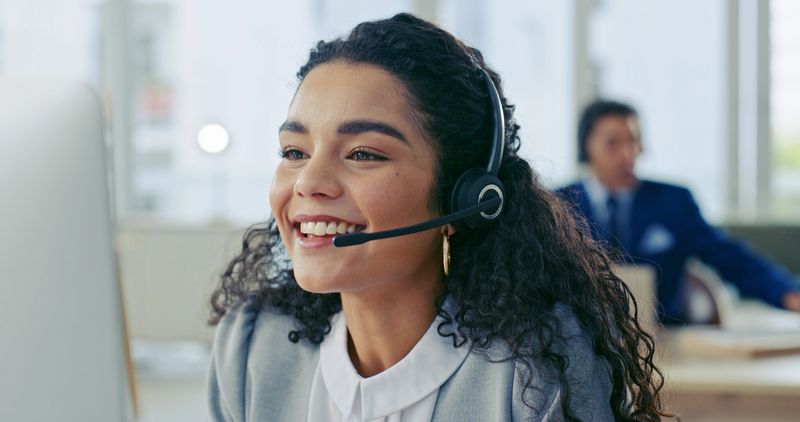 Friendly customer service representative wearing a headset, cheerfully assisting clients in a busy office environment, embodying professionalism and effective communication.