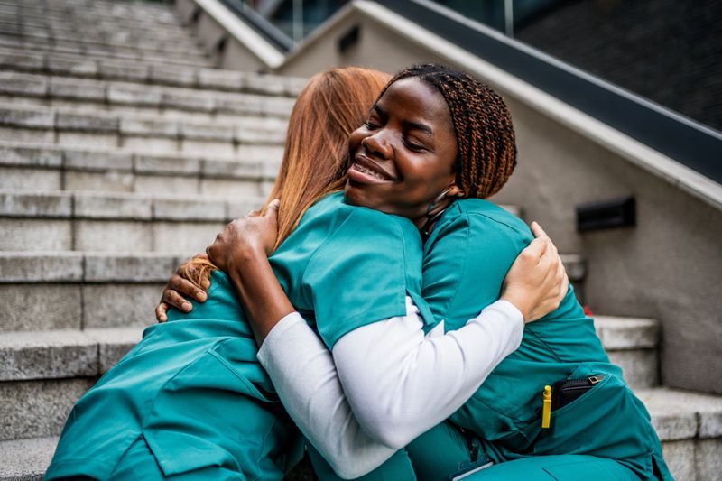 Two multiethnic female nurses are embracing each other, providing emotional support after a challenging day