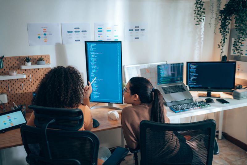 Diversity Female software developers collaborating on code review at tech workstation