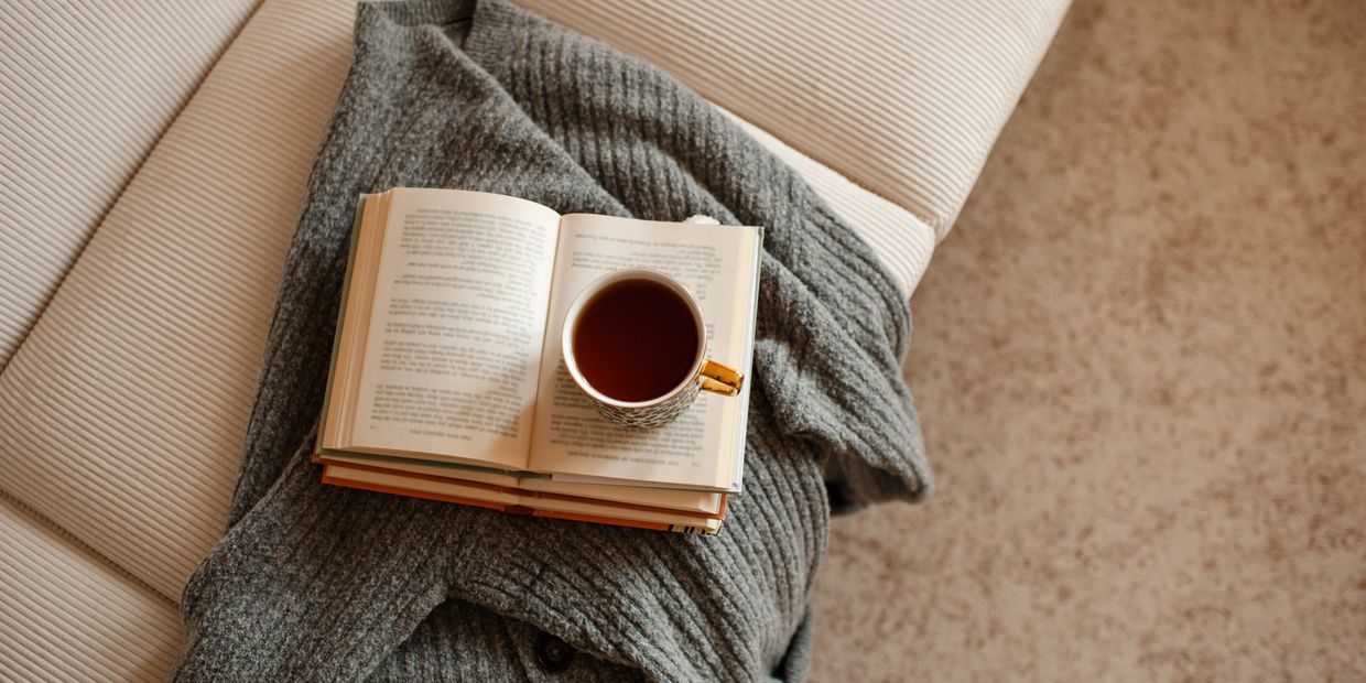 Cozy scene with a gray sweater, open book, and a cup of tea on a beige couch.