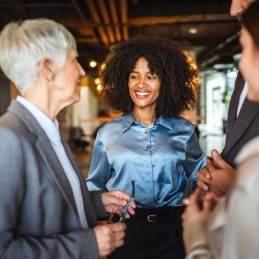 Smiling businesswoman in a blue blouse engaging in conversation with colleagues.
