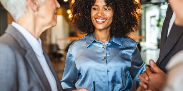 Smiling businesswoman in a blue blouse engaging in conversation with colleagues.