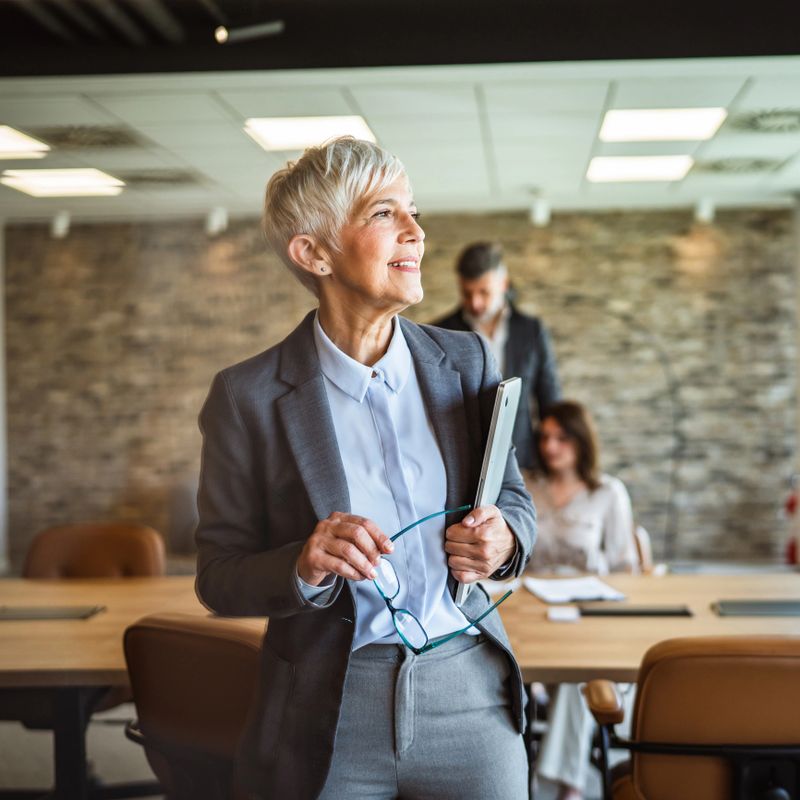 pretty aged businesswoman hold laptop in arms and smile at workplace