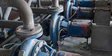 Row of industrial blue pumps connected to large gray pipes in a factory setting.