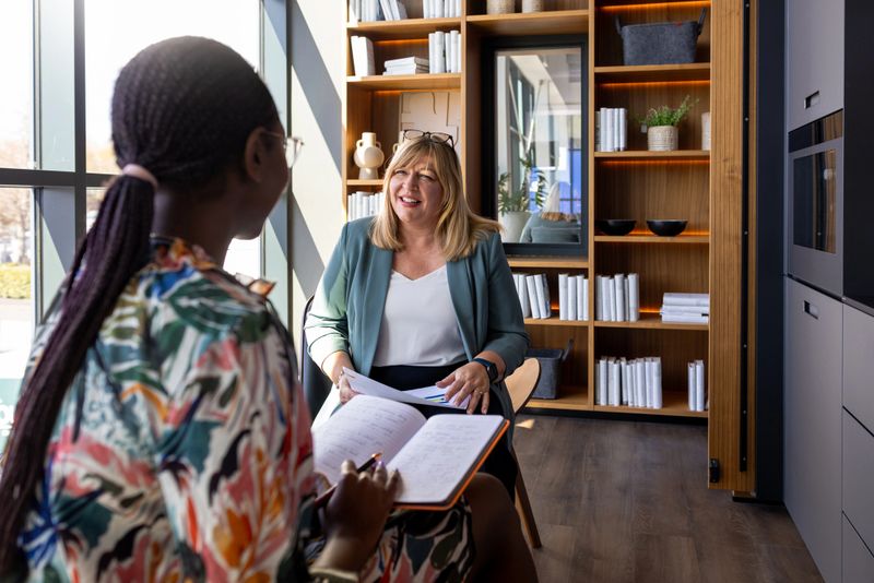 A medium over the shoulder shot of two professional women engaging in a friendly and productive business discussion in a stylish, modern office with large windows and natural lighting. One woman is attentively taking notes while the other speaks and smiles warmly. The scene conveys collaboration, mentorship, and effective communication in a contemporary workspace.

Videos are available similar to this scenario.