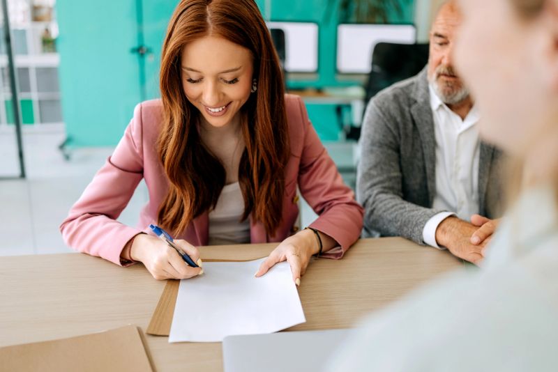 Young woman signing document during team meeting at modern board room