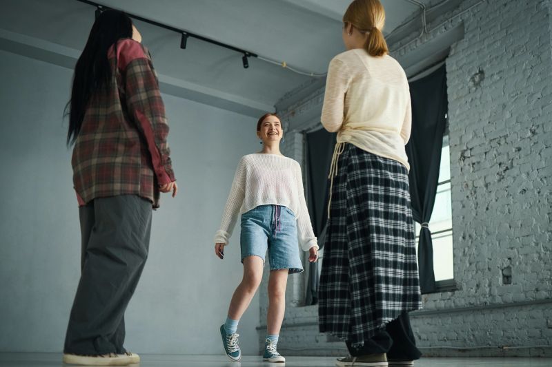 Smiling young woman enjoying dance class with other participants in studio with brick walls and large windows. Wearing casual clothes for comfortable movement