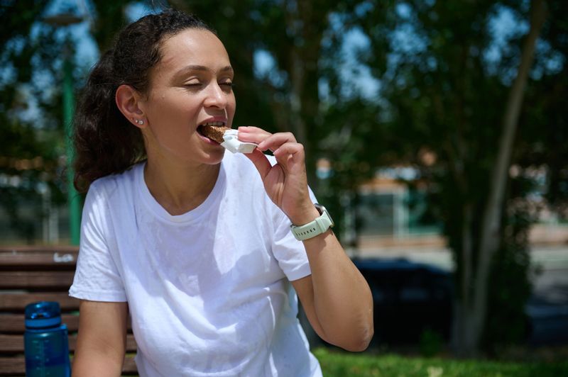 A woman is savoring a healthy snack while outdoors on a sunny day, showcasing enjoyment and wellness in an active lifestyle. The scene evokes happiness and vitality in nature.