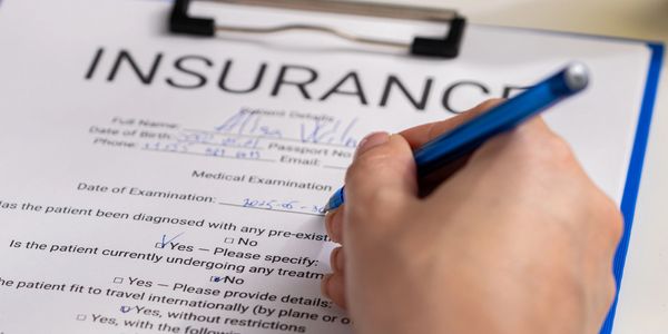 A person filling out an insurance medical examination form with a blue pen.