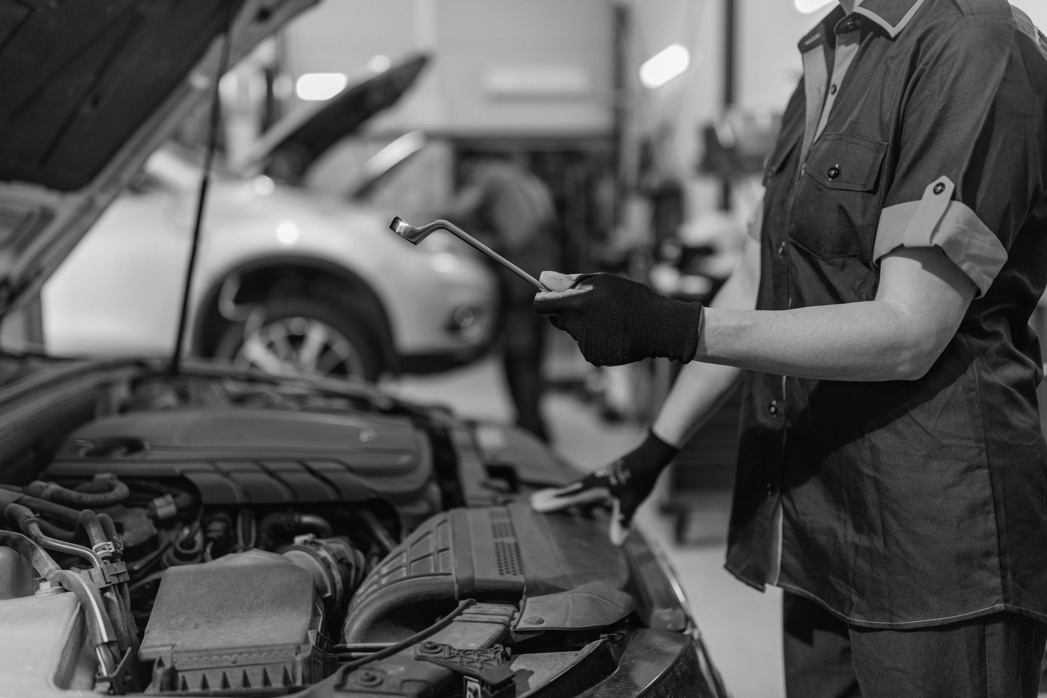 Mechanic holding a tool near an open car hood in a repair shop.