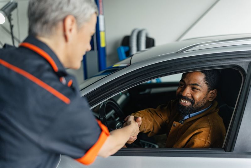 A mechanic and a customer share a friendly handshake inside an auto service garage, exemplifying great customer service and trust in the automotive repair industry.