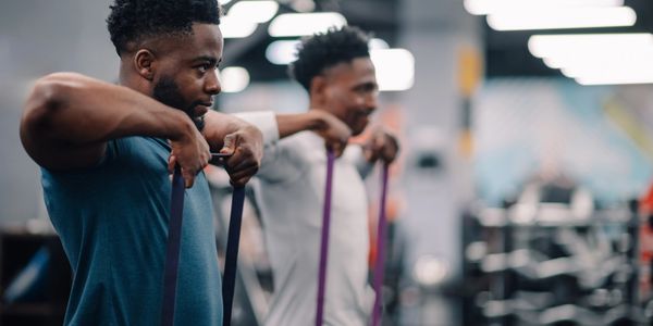 Two men exercising with resistance bands in a gym.