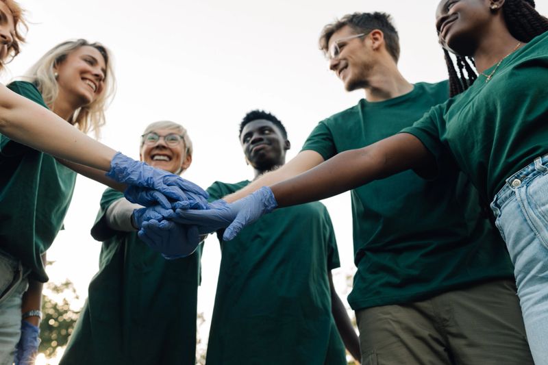 Volunteers wearing matching t-shirts and protective gloves join hands, demonstrating teamwork and community spirit