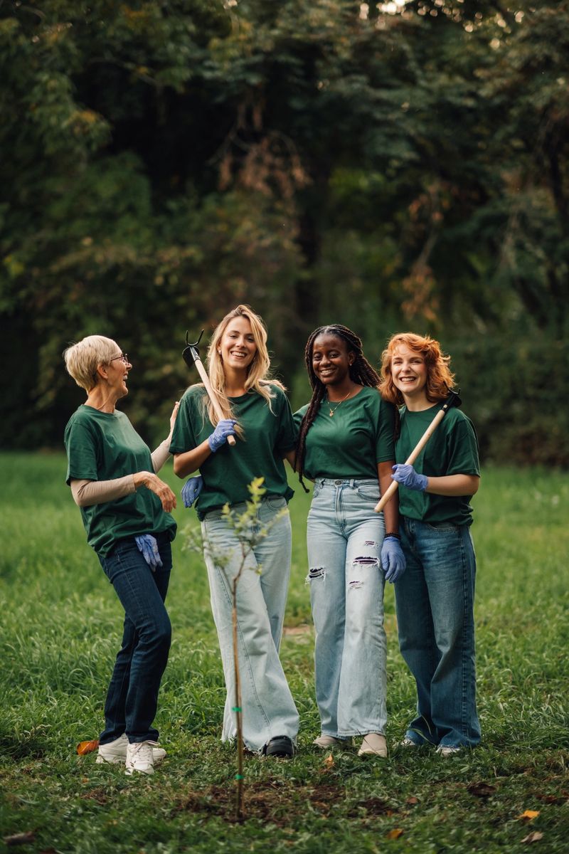 Four female volunteers smiling and looking at the camera while planting a tree in a public park, contributing to community sustainability efforts