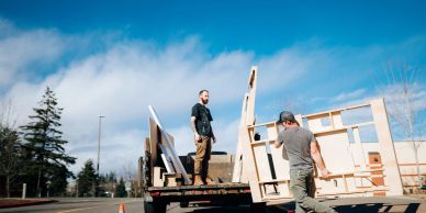 Two men unloading wooden boards from a truck.