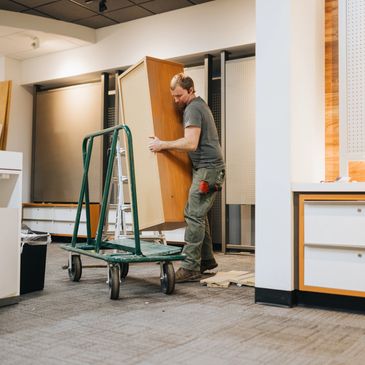 Man moving a wooden cabinet inside a room with a dolly cart.
